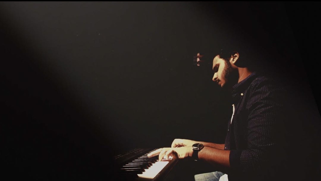 Ahmed Mitry at the piano in a dark studio